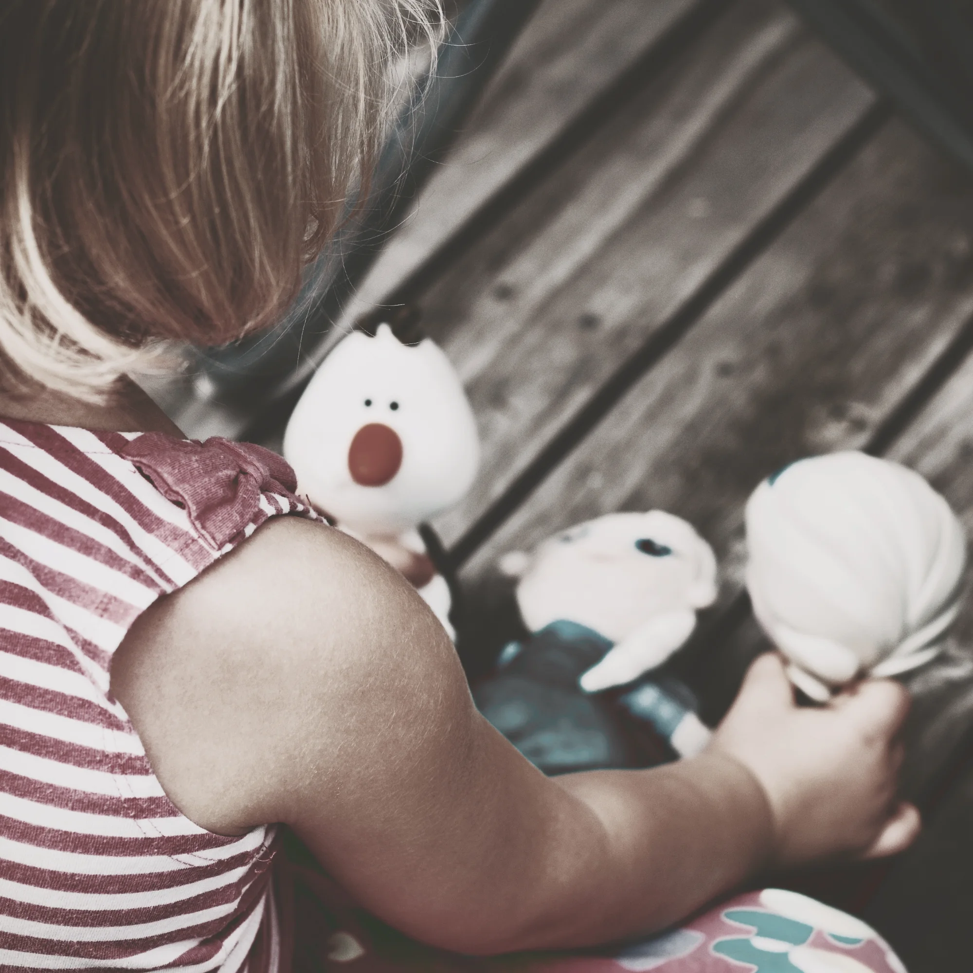 A small child, seen from behind, gently absorbed in play with soft toys