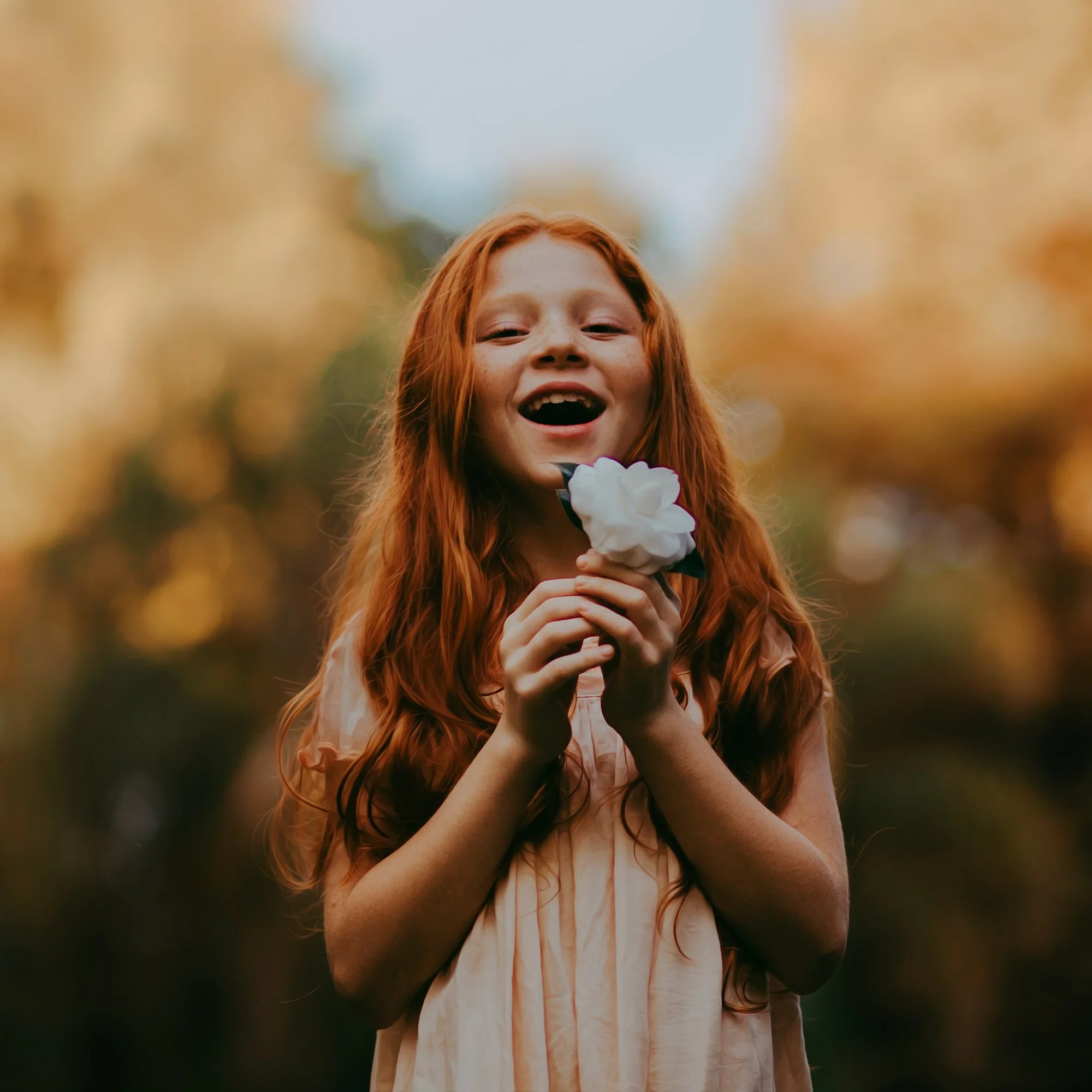 A young girl laughing in golden light, holding a single white flower