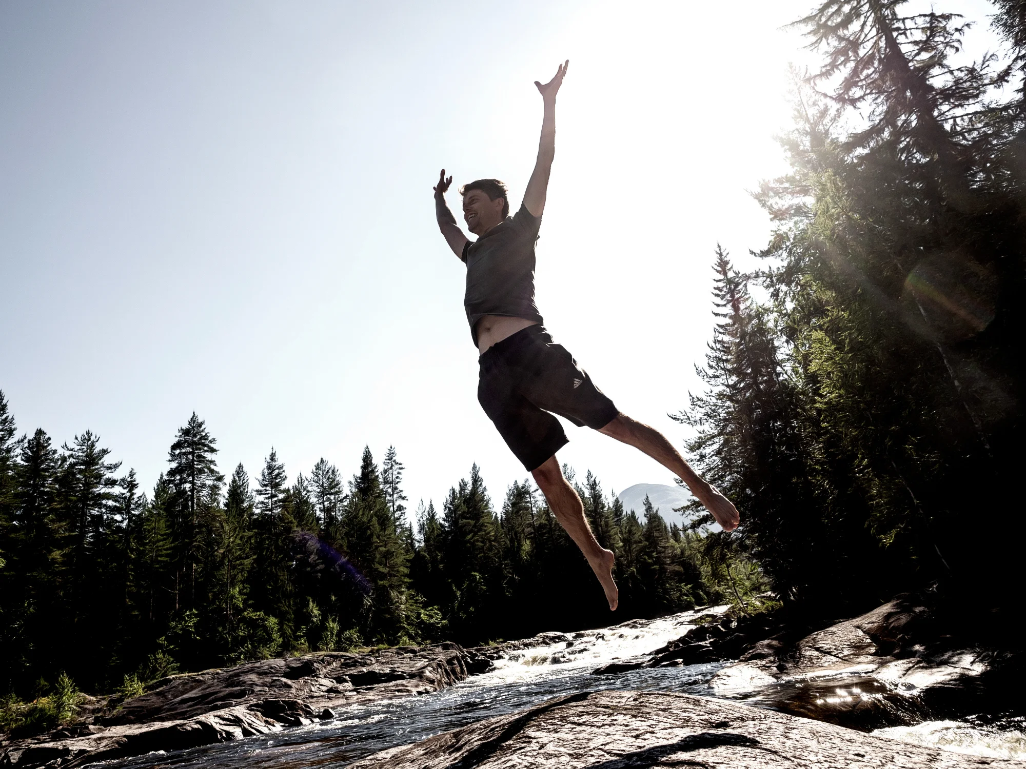 Jacob leaping beside a mountain river at golden hour, arms flung wide.